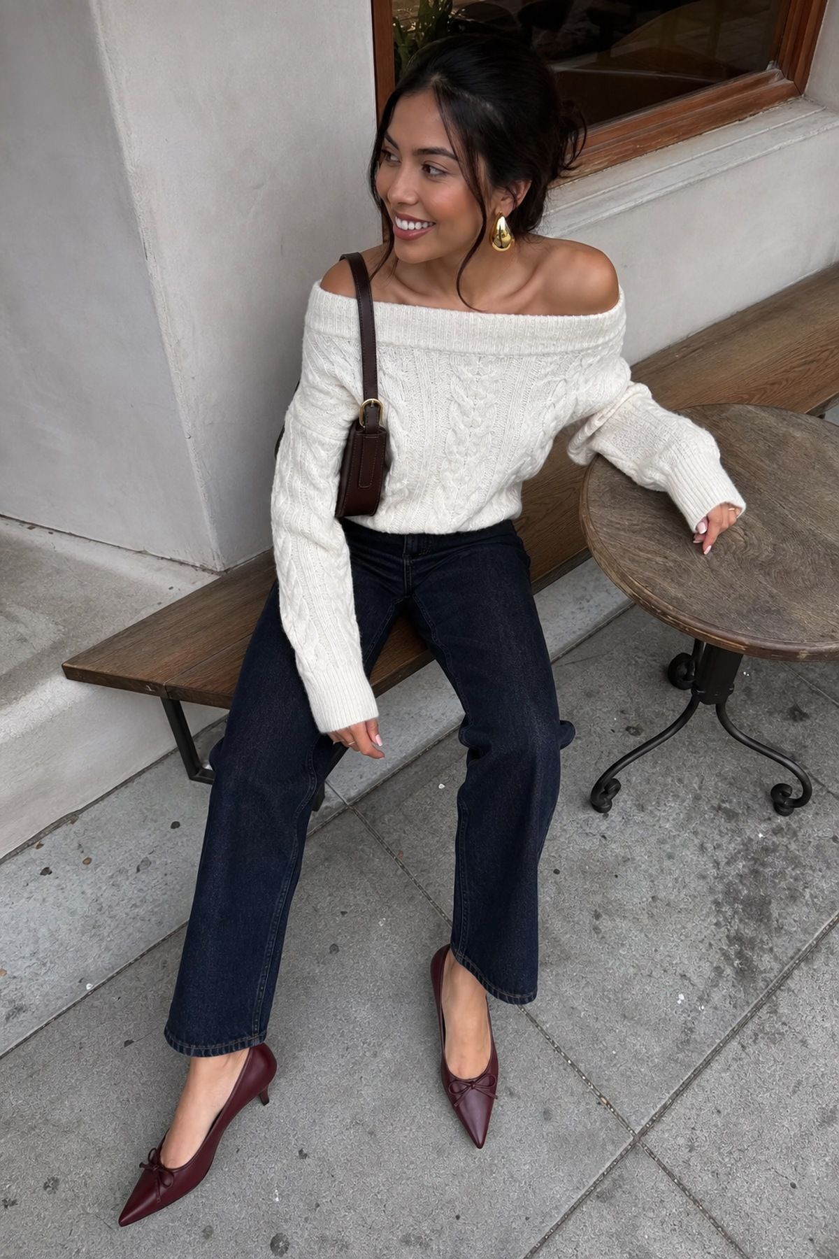 Woman wearing an off-shoulder sweater with dark jeans and heels, a casual Christmas party outfit