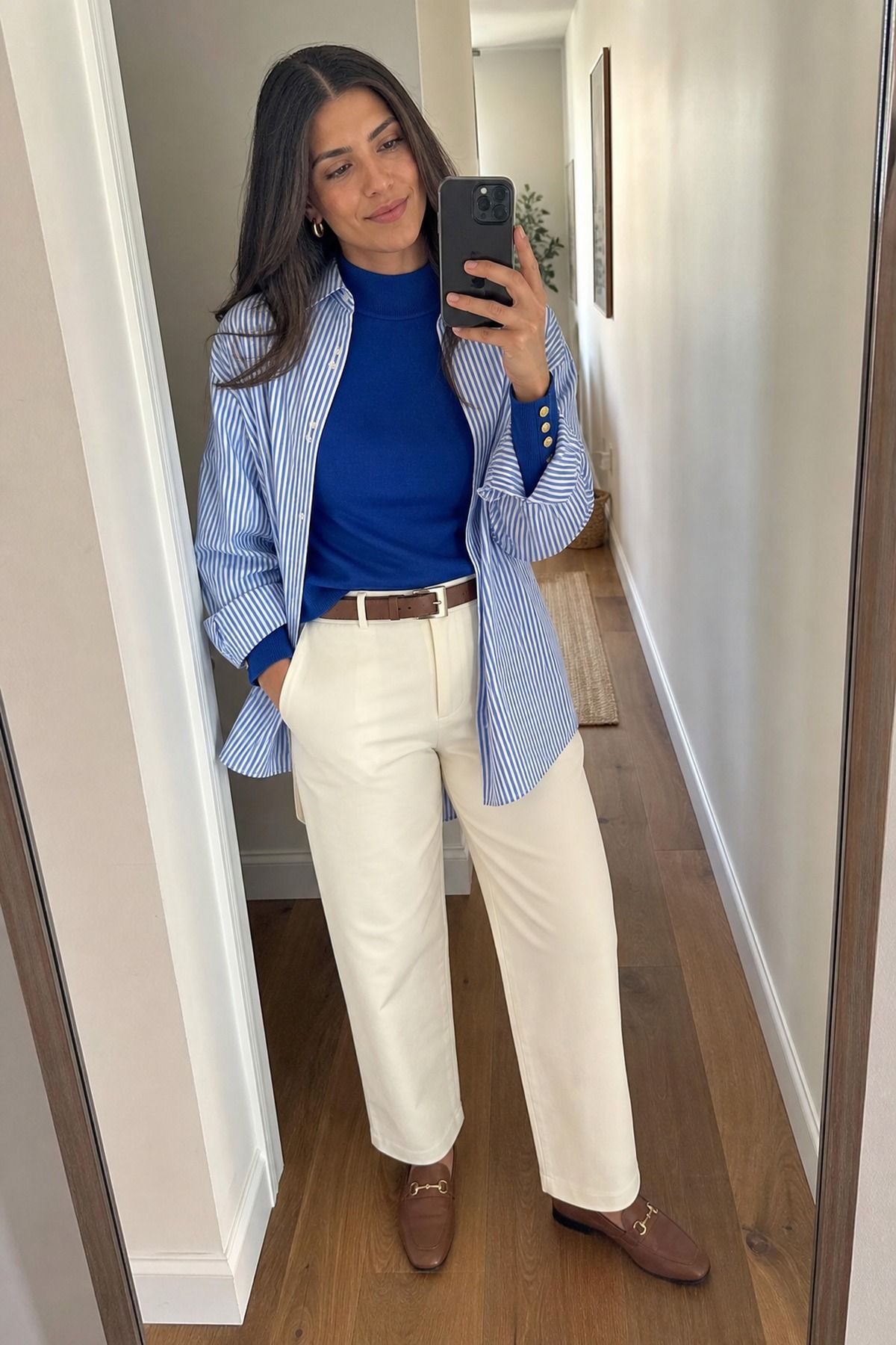 Woman wearing a royal blue mock neck with gold buttons and a striped button-down