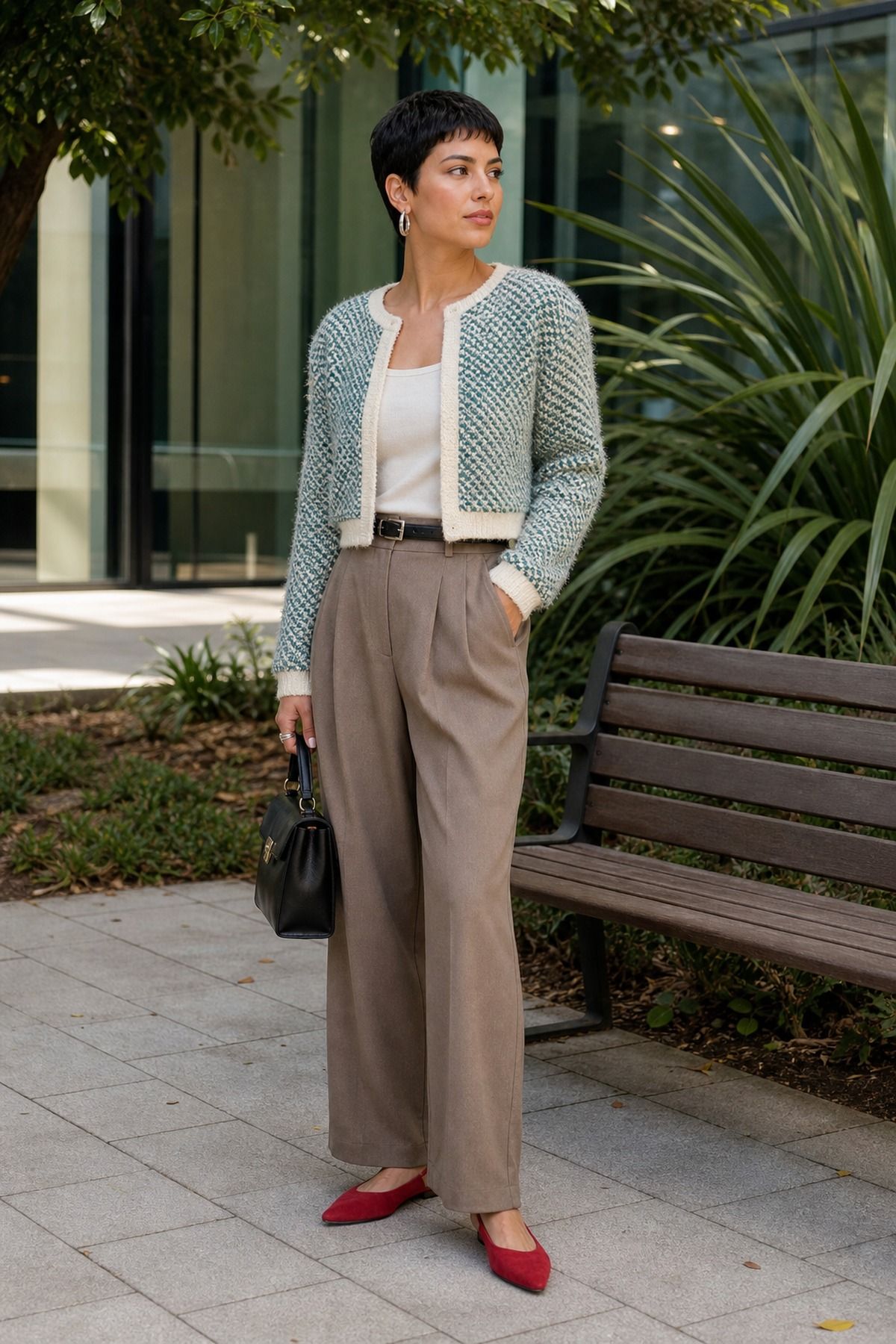 Woman in a teal and cream textured cardigan jacket with trim over a white top, taupe trousers, red pointed flats and a black bag