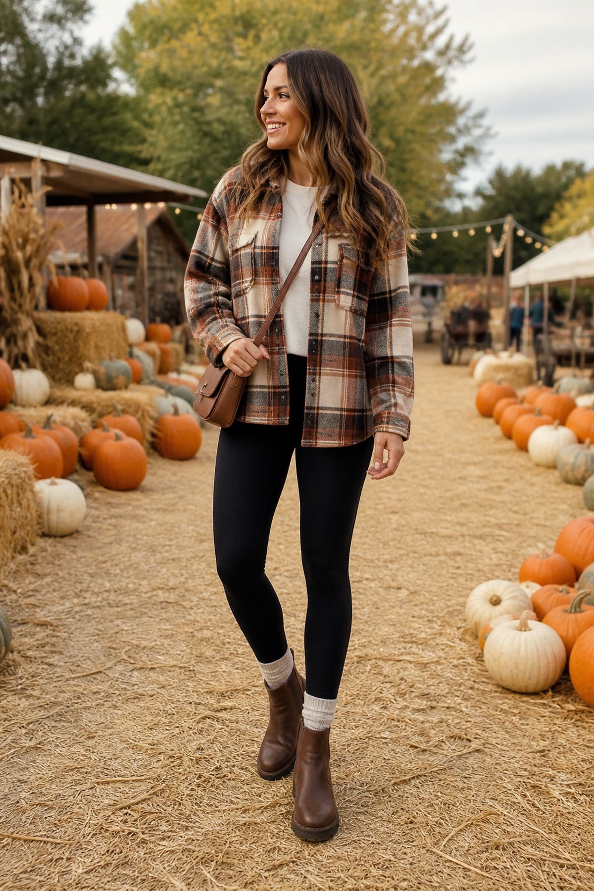 Woman in a brown plaid shacket, white tee, black leggings and brown lace-up boots walking on straw at a pumpkin patch