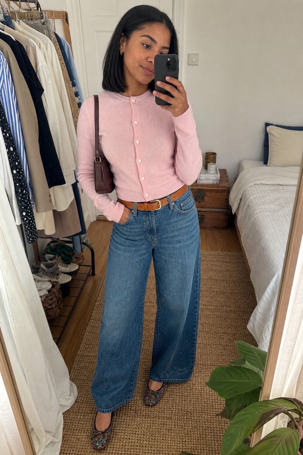 Mirror selfie of a woman in a pink cardigan buttoned and tucked into wide-leg jeans with a brown belt, leopard flats and a brown bag