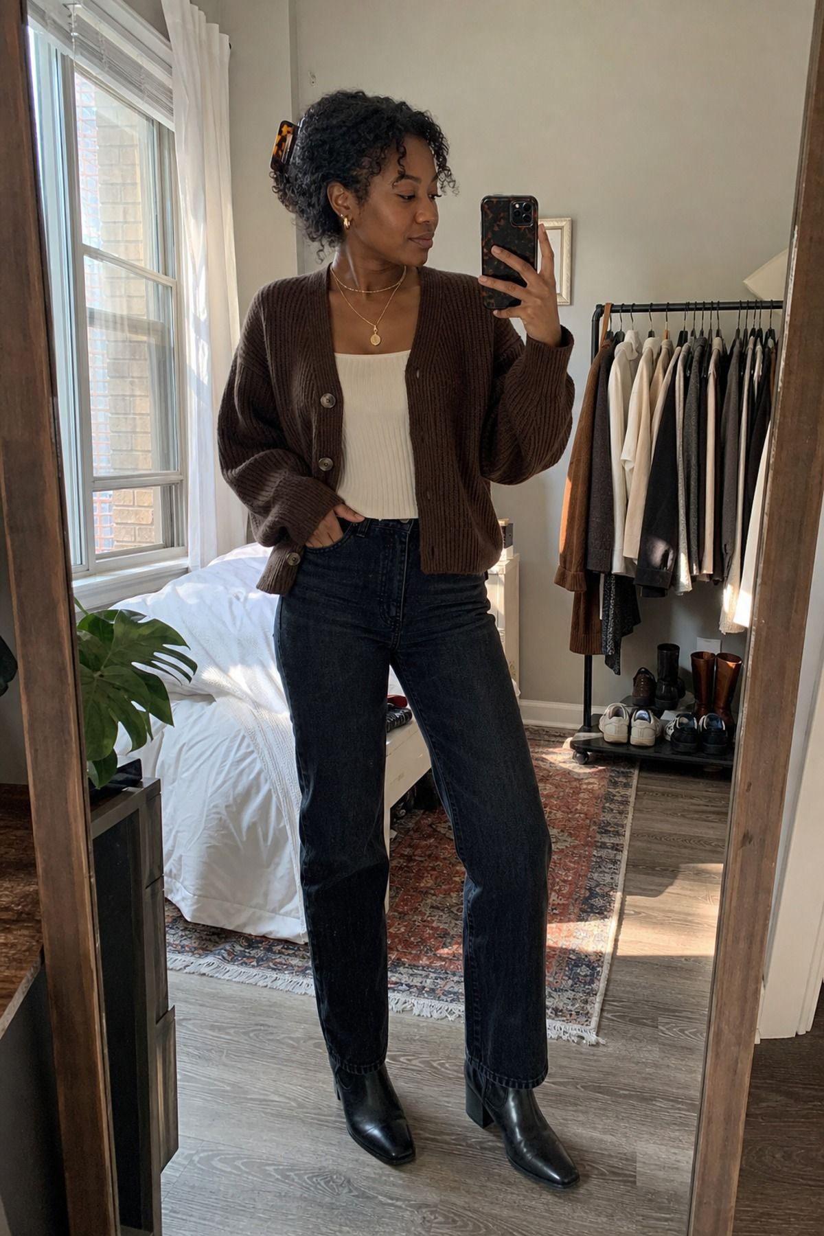 Woman in an open chocolate brown cardigan over a cream top with dark straight jeans and black ankle boots in a mirror selfie