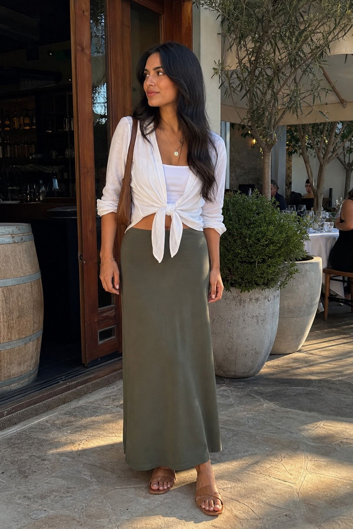 Woman in a white tie-front blouse, sage green maxi skirt and tan sandals on a restaurant patio
