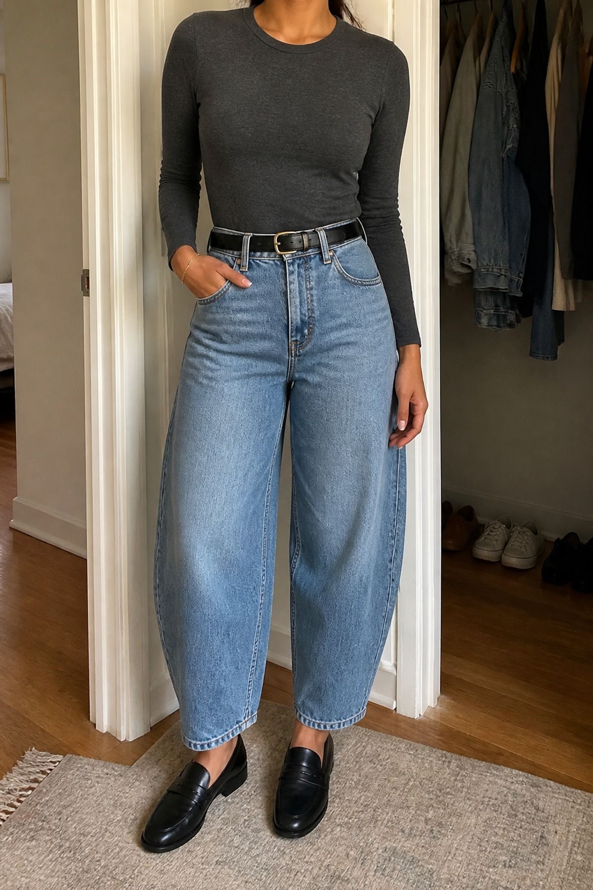 Woman in a charcoal fitted long-sleeve tee, black belt, light-wash barrel jeans and black loafers in a doorway