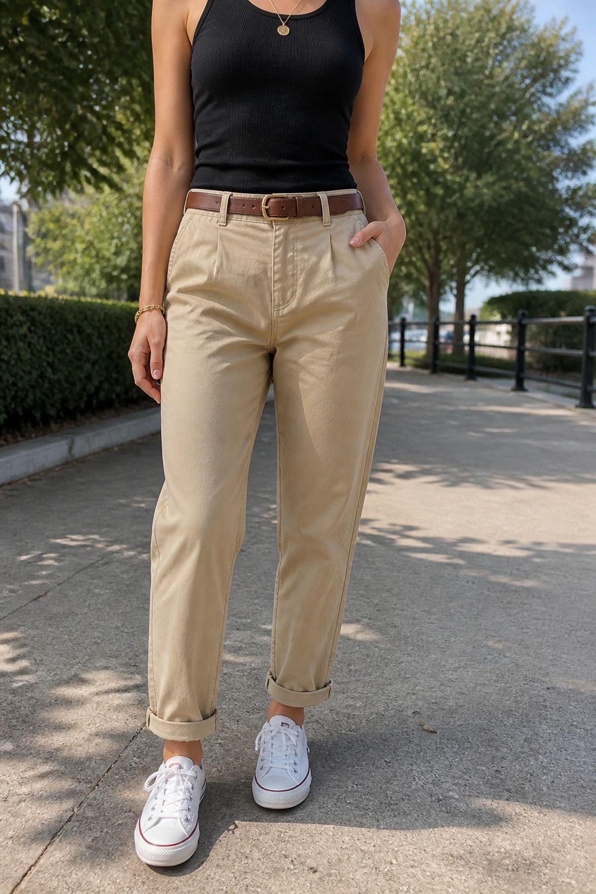 Woman in a black fitted tank, brown belt, khaki relaxed chinos with cuffed hems and white canvas sneakers on a sidewalk