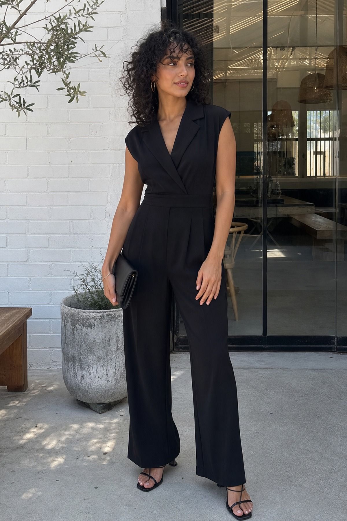 Woman wearing a black jumpsuit with minimal sandals, an all black outfit